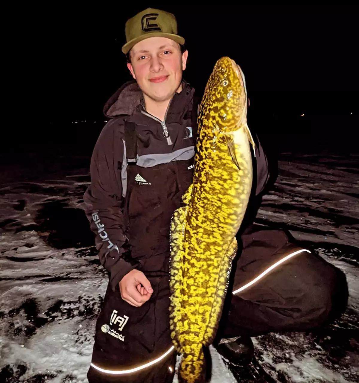 An ice fisherman holds a large burbot at night. 